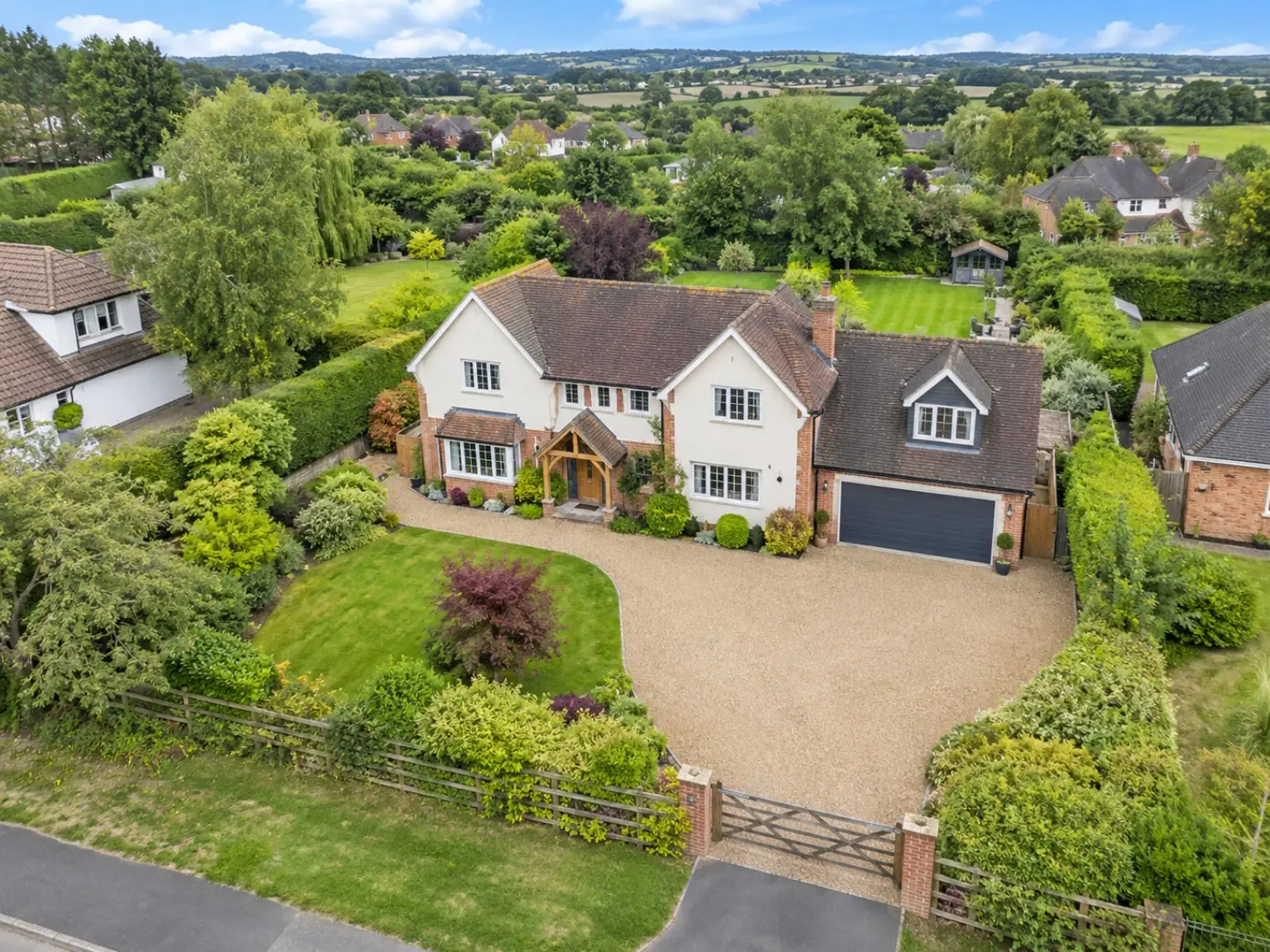 Aerial photograph of a detached house with a gravel driveway, gardens and open countryside behind