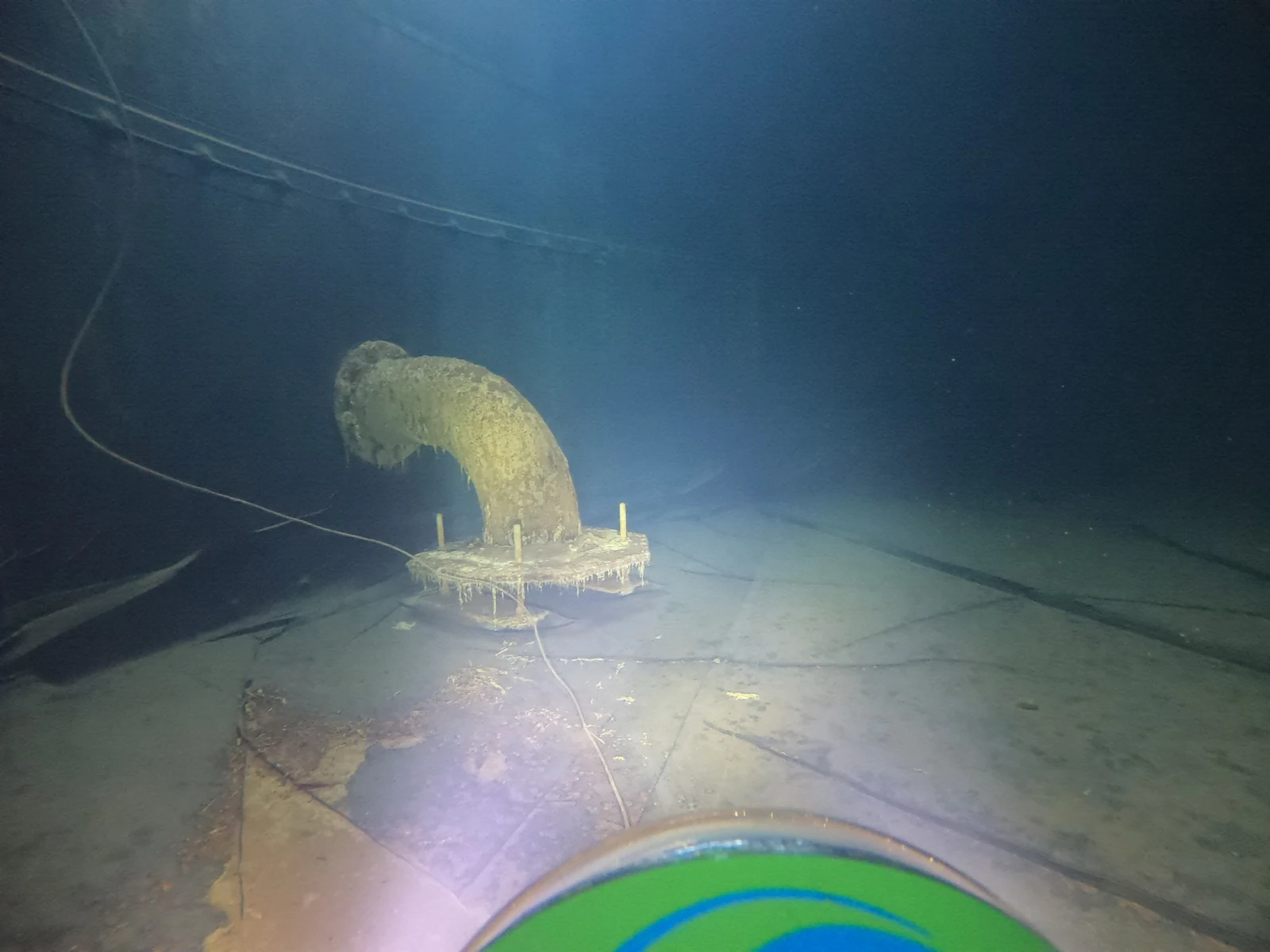 Underwater inspection image showing a pipe outlet, tank liner and sediment on the floor