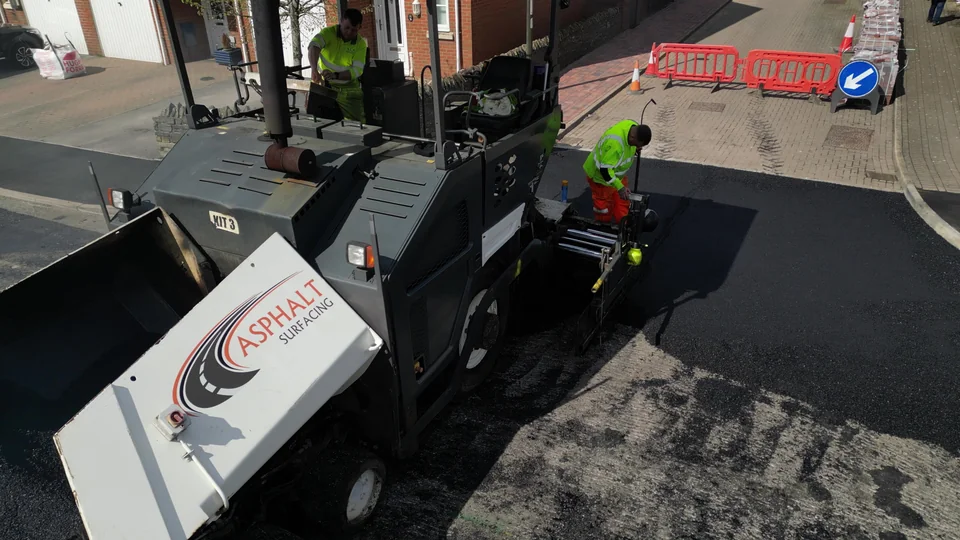 Paving equipment, road workers and traffic barriers on a residential street