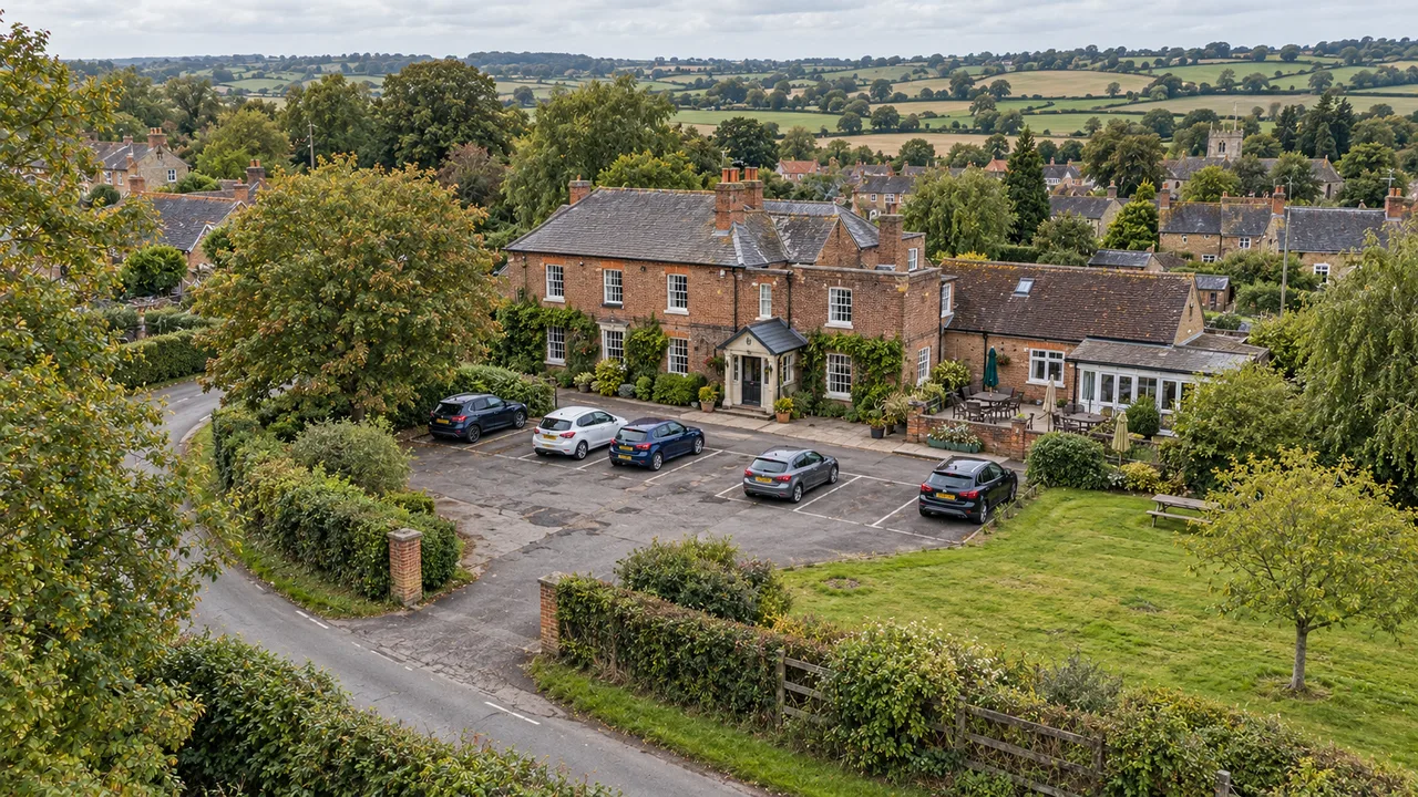 Aerial view of a brick country inn with a car park, entrance drive and village surroundings