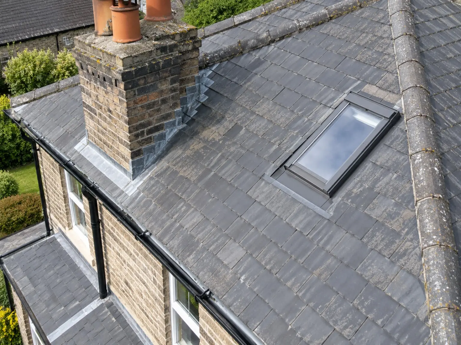 Close aerial view of a slate roof showing a chimney, rooflight, lead flashing and guttering